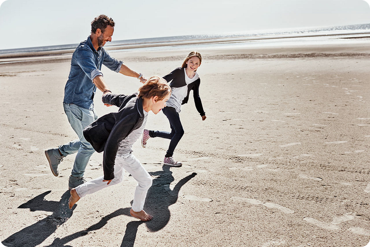 Ein Vater rennt mit seinen Kindern lachend und glücklich am Strand