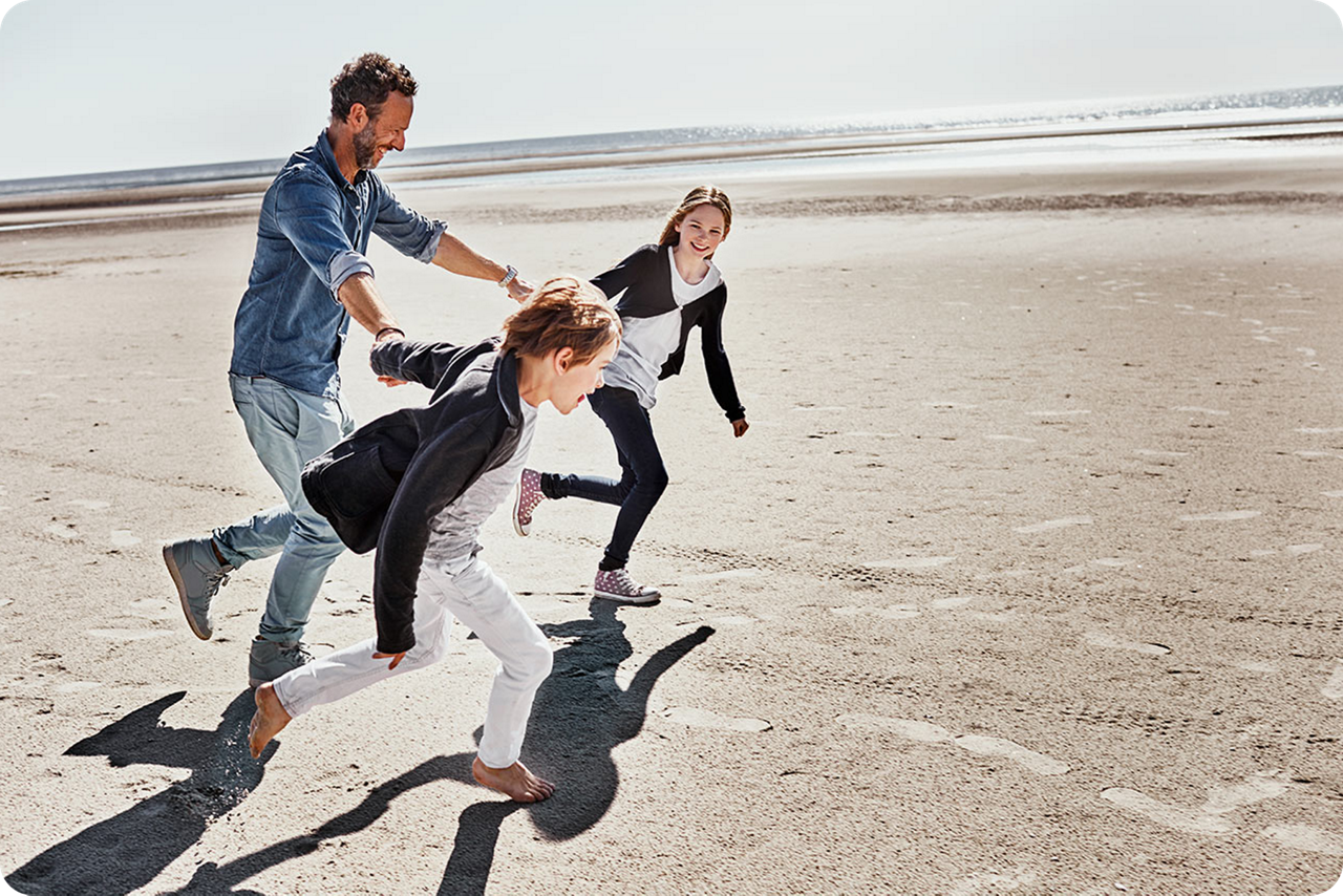Ein Vater rennt mit seinen Kindern lachend und glücklich am Strand