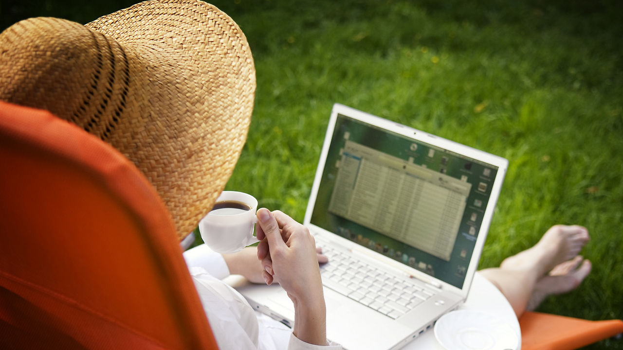Frau sitzt im Liegestuhl und schaut auf einen Laptop