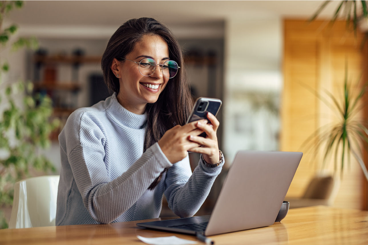 Junge Frau am Tisch schaut lächelnd auf ihr Smartphone