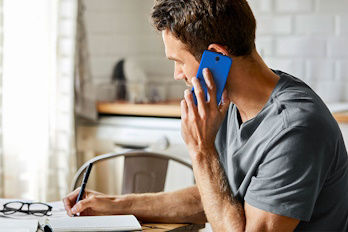 Mann telefoniert mit dem Handy und macht sich Notizen