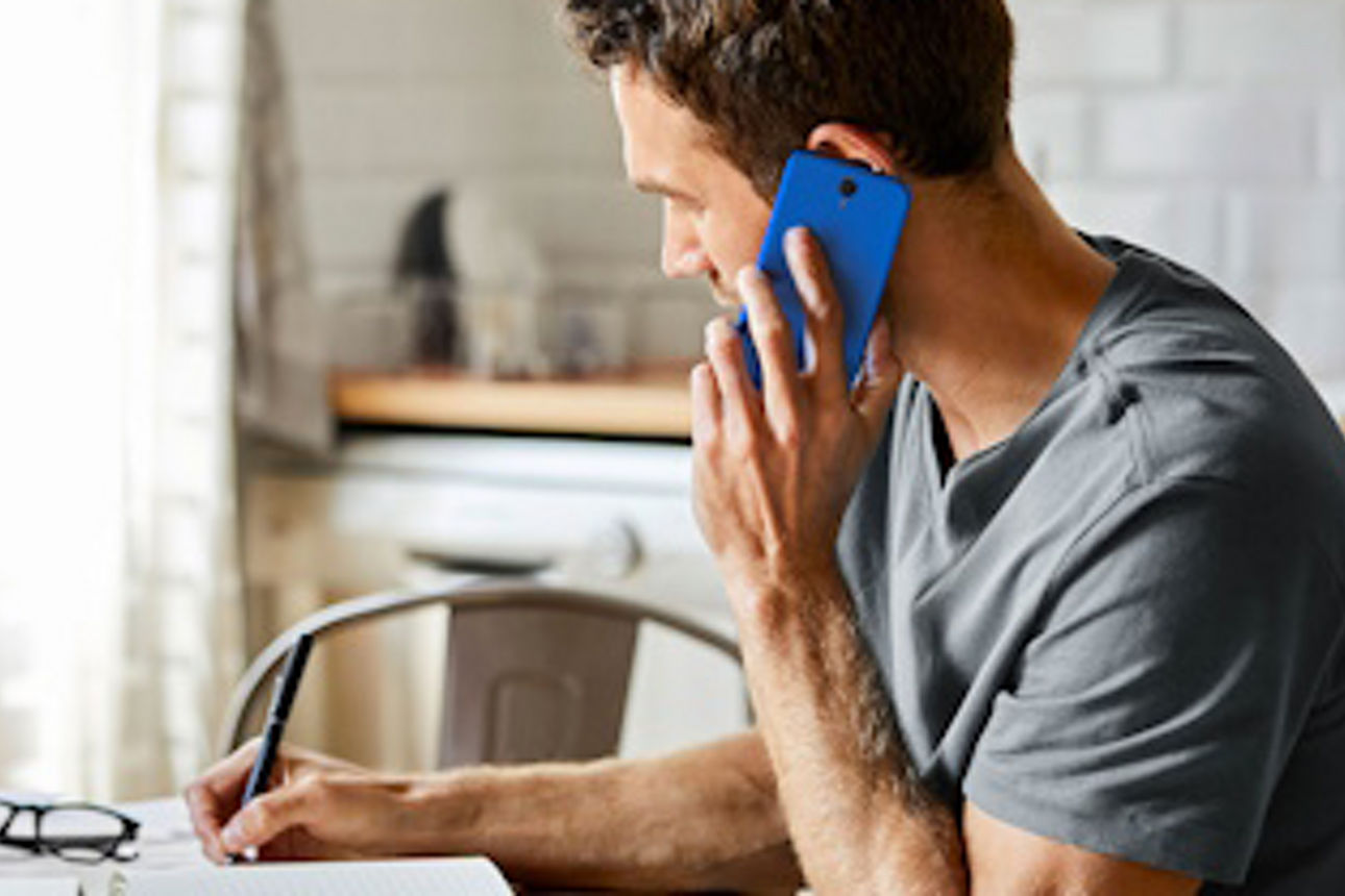 Mann telefoniert mit dem Handy und macht sich Notizen