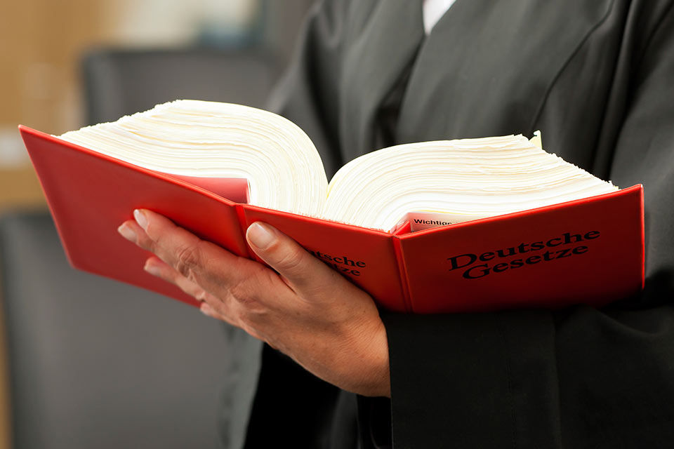 Eine Hand hält ein aufgeklapptes, rotes Gesetzbuch. 