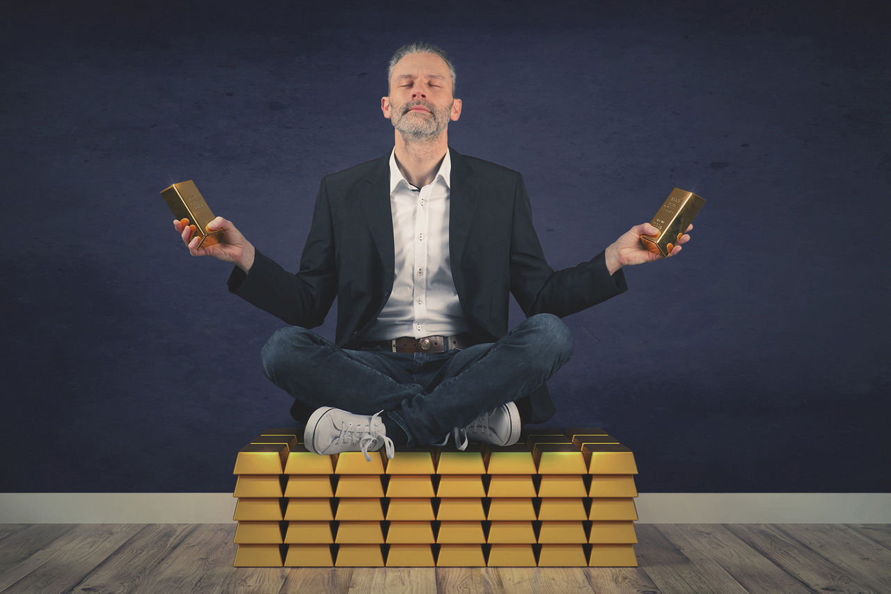 Mann sitzt auf Goldbarren