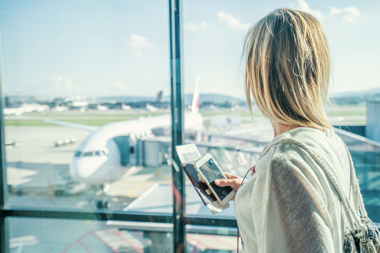 Frau steht am Flughafen und guckt auf ein stehendes Flugzeug