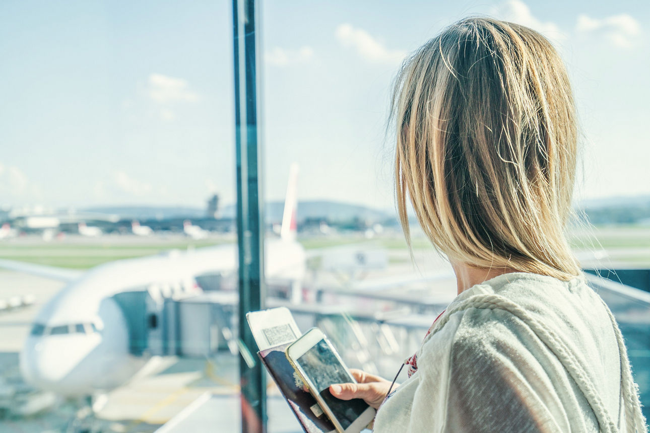 Frau steht am Flughafen und guckt auf ein stehendes Flugzeug