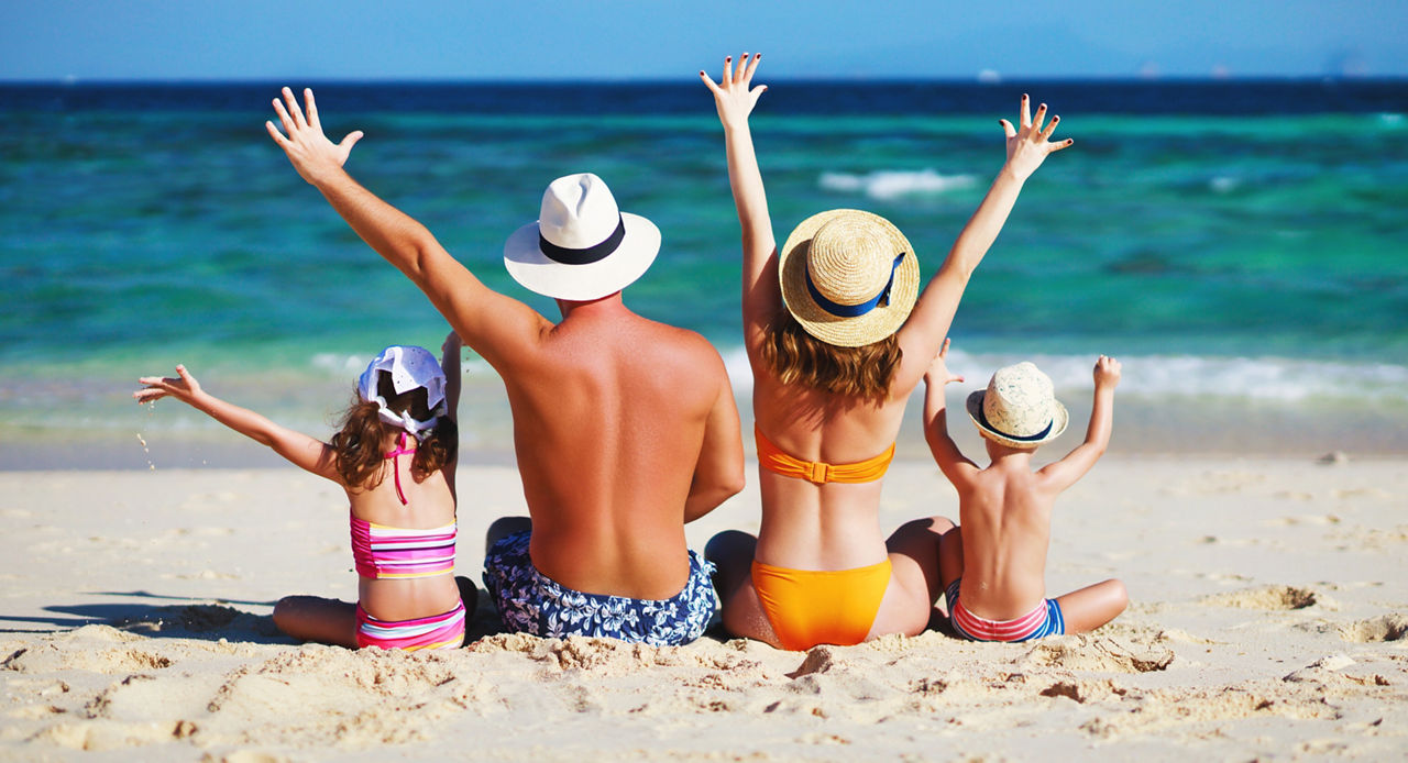Glückliche Familie: Vater, Mutter und Kinder mit dem Rücken zur See am Strand