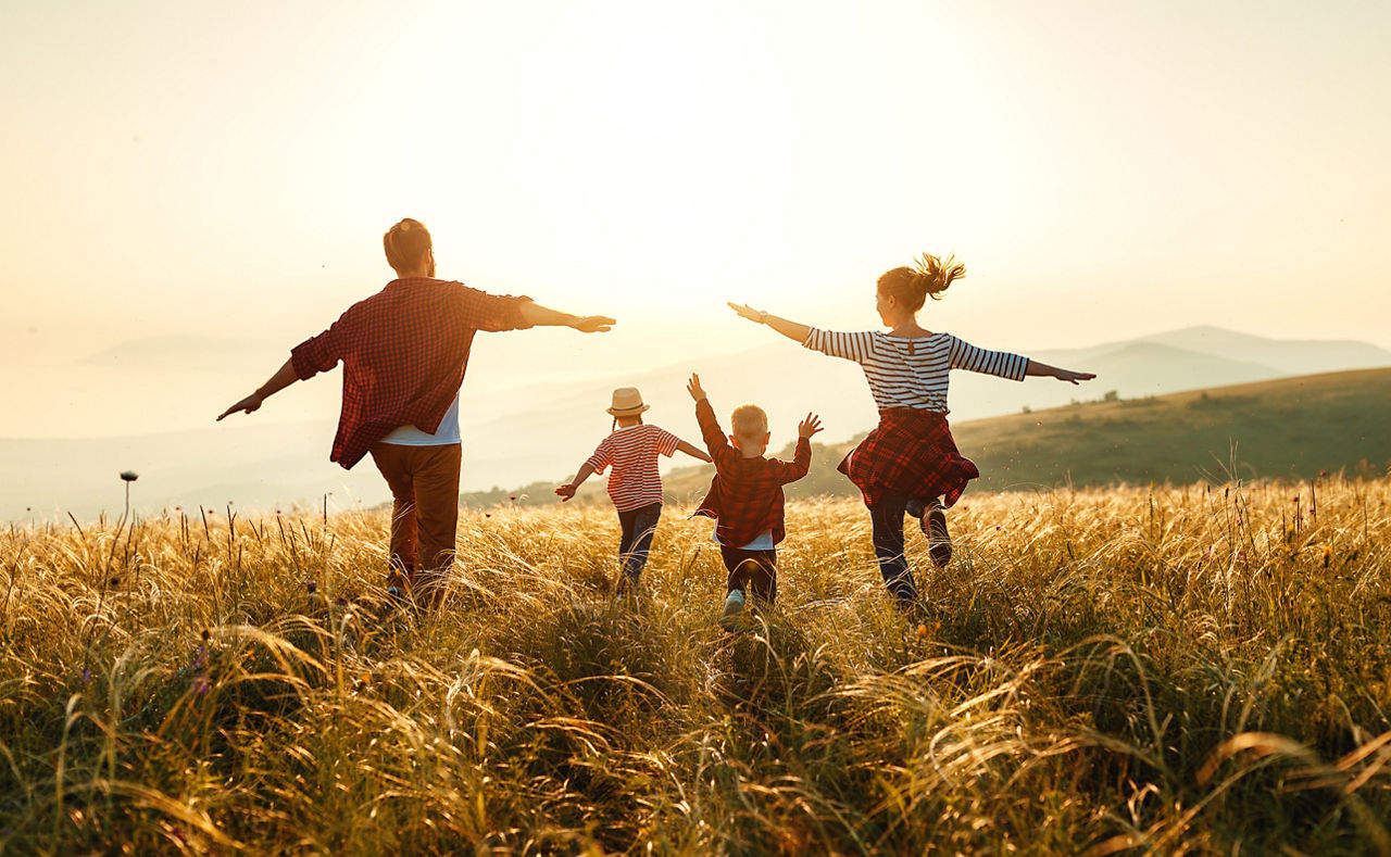 Eltern und zwei Kinder rennen richtung Sonnenuntergang
