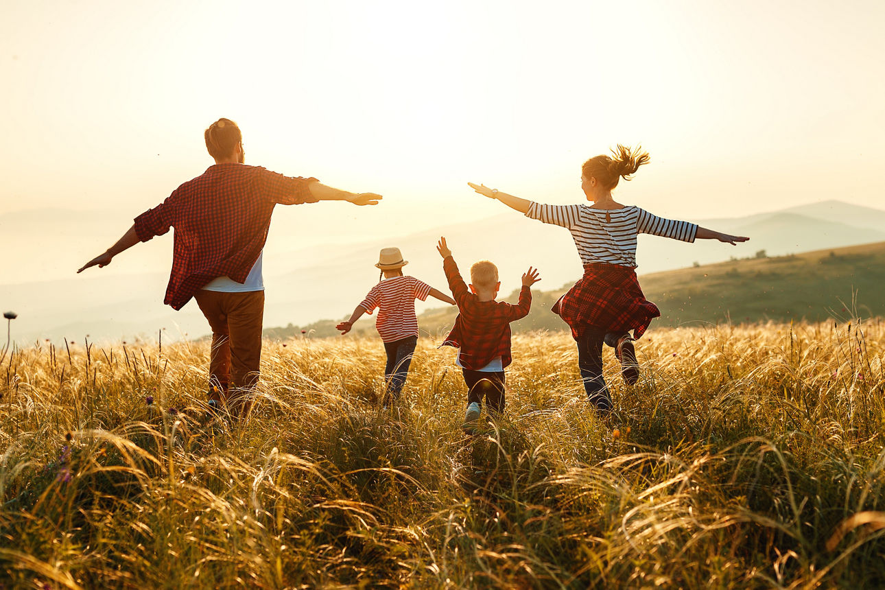 Eltern und zwei Kinder rennen richtung Sonnenuntergang