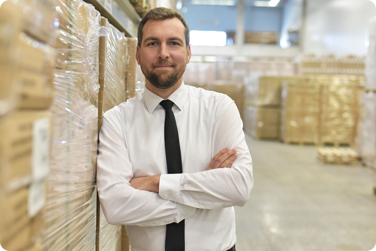 Ein Unternehmer steht im Warenlager an Paletten angelehnt