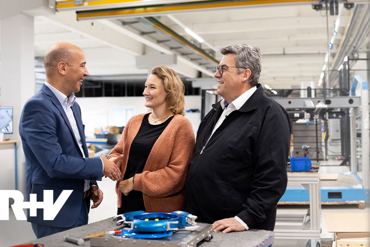 Drei Menschen stehen in einer Produktionshalle und schütteln sich die Hände