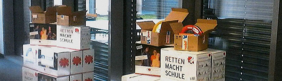 Kisten mit der Aufschrift "Retten macht Schule", gestapelt in der Nähe eines Fensters