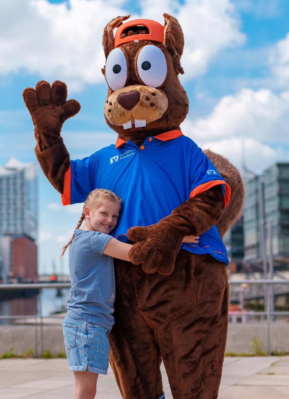 Richy Reichhörnchen in blauem Shirt und orangefarbener Mütze winkt, ein Kind umarmt Richy vor städtische Kulisse.