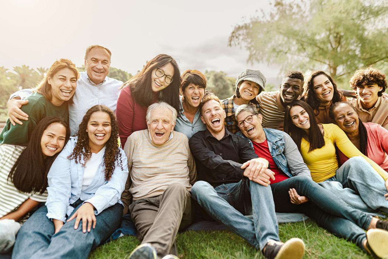 Viele Meschen sitzen und lachen zusammen auf einer Wiese 