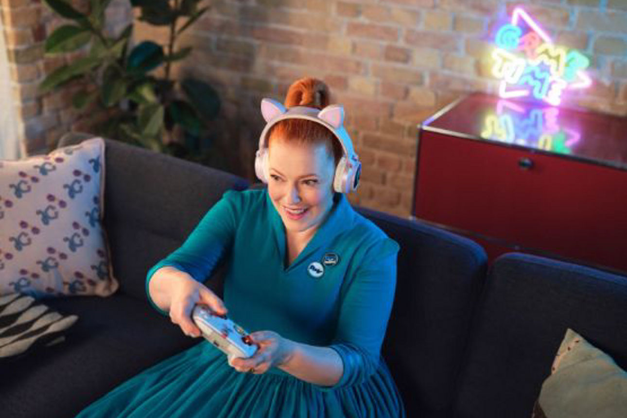 Frau sitzt lachend auf der Couch mit Controller in der Hand
