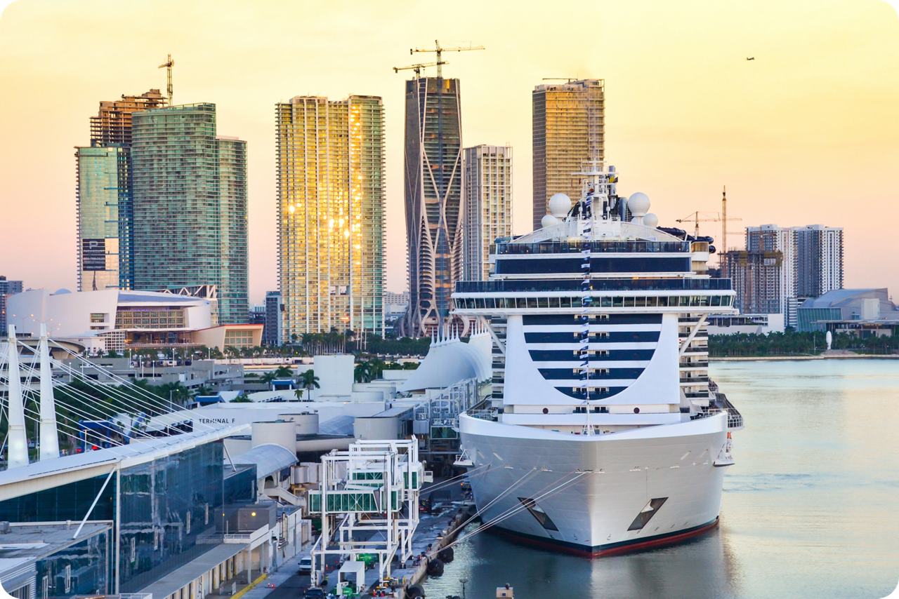Großes Kreuzfahrtschiff im Hafen vor moderner Skyline mit Hochhäusern.