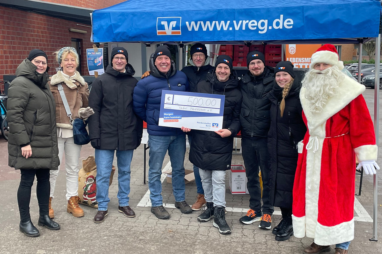 Viele Personen stehen im Freien neben einem Pavillon auf dem Supermarkt-Parkplatz. Ein Mann ist als Nikolaus verkleidet.