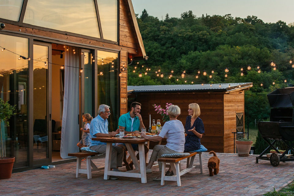 Familie sitzt am Tisch auf einer Teresse beim Grillen