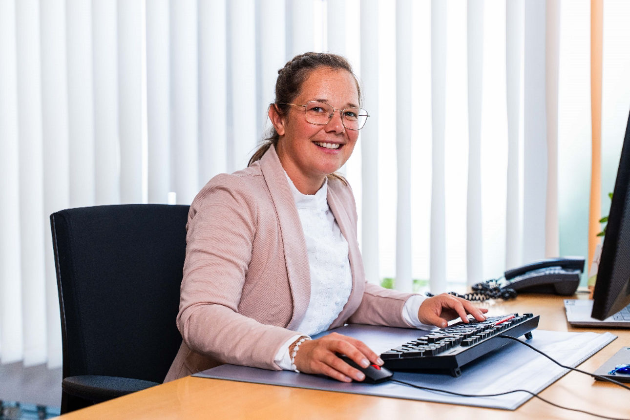 Eine lächelnde Frau sitzt an ihrem Arbeitsplatz