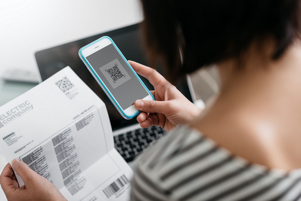 Woman checkiEine Frau scannt mit ihrem Handy den QR-Code auf einer Rechnung.ng an electricity bill, she is making a contactless payment using her smartphone