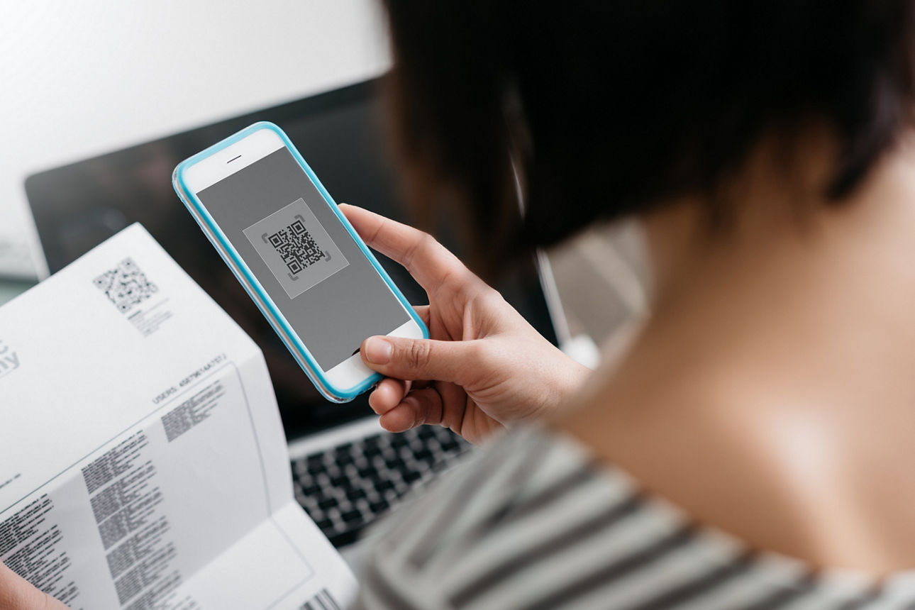 Eine Frau scannt mit ihrem Handy den QR-Code auf einer Rechnung. Woman checkiEine Frau scannt mit ihrem Handy den QR-Code auf einer Rechnung.ng an electricity bill, she is making a contactless payment using her smartphone