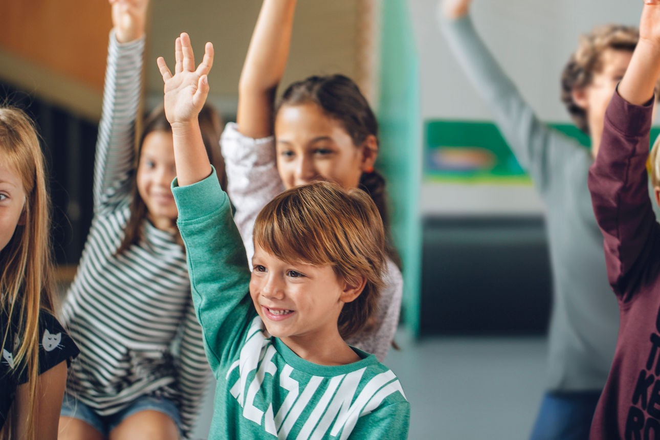 Kinder in einem Schulklassenraum strecken den Arm nach oben.