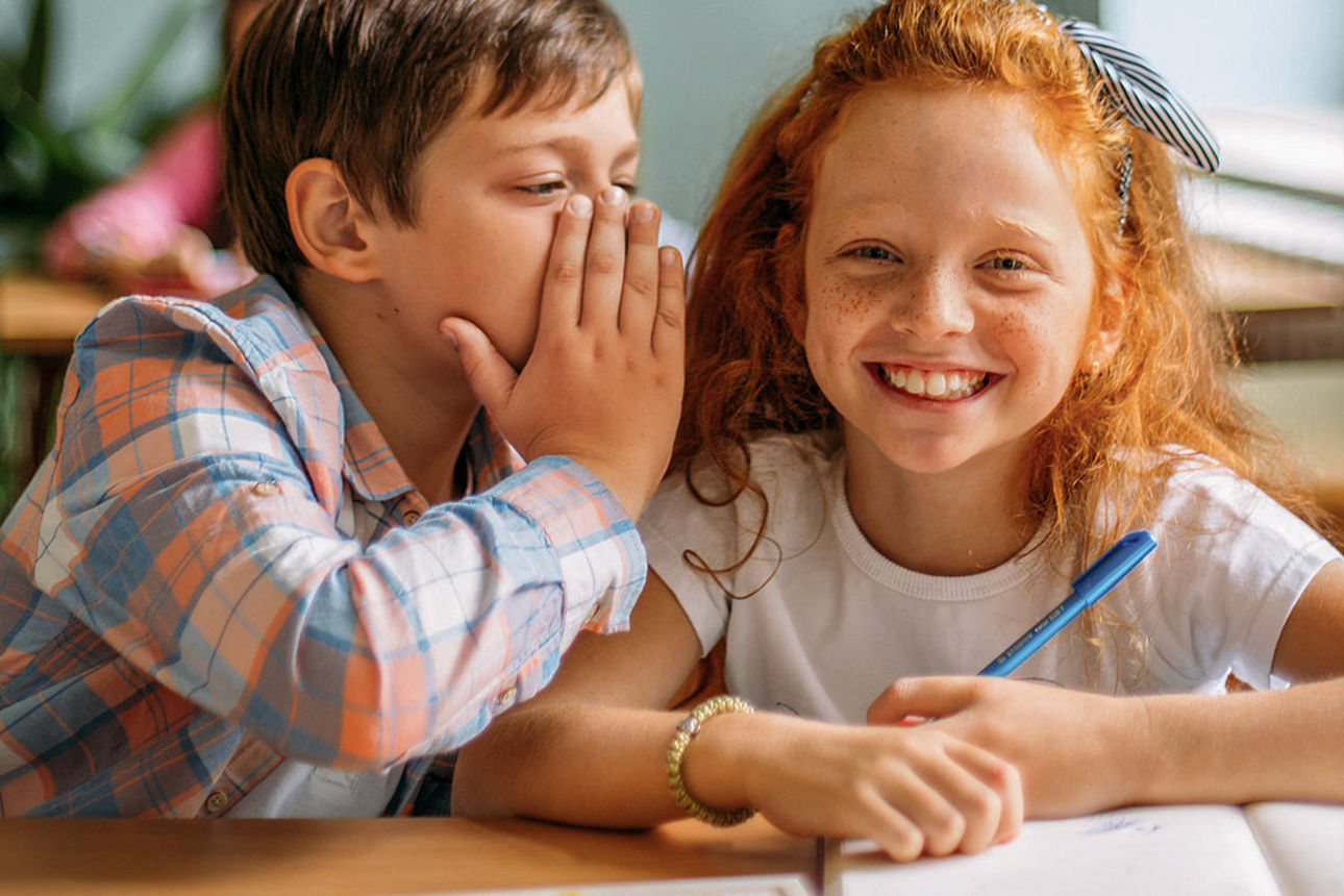 Ein Mädchen und ein Junge sitzen mit Globus, Buch und Steckspiel an einem Tisch.