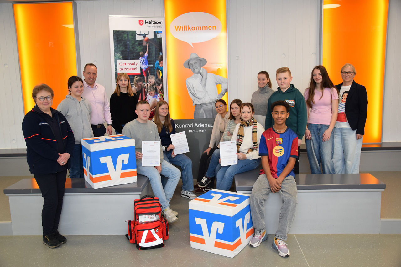 Auf dem Bild ist eine Gruppe von Jugendlichen und Erwachsenen in einem modernen Innenraum zu sehen.