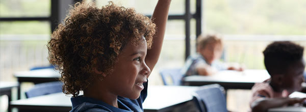Ein Kind im Klassenzimmer hebt die Hand, um eine Frage zu beantworten oder sich am Unterricht zu beteiligen. 