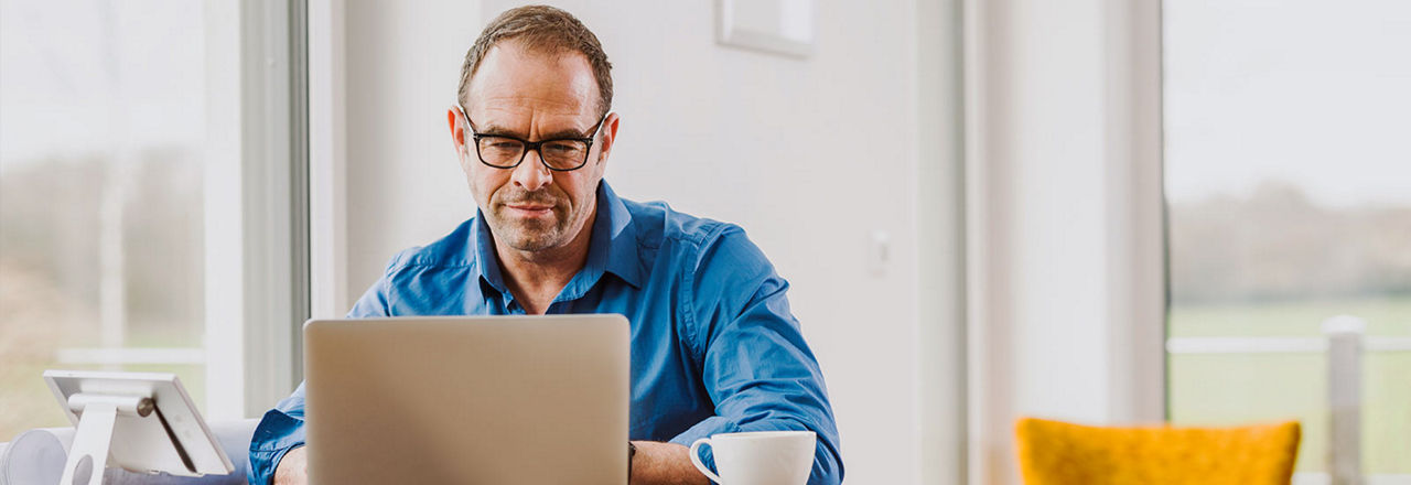 Mann mit Brille im blauen Hemd am Tisch mit Laptop
