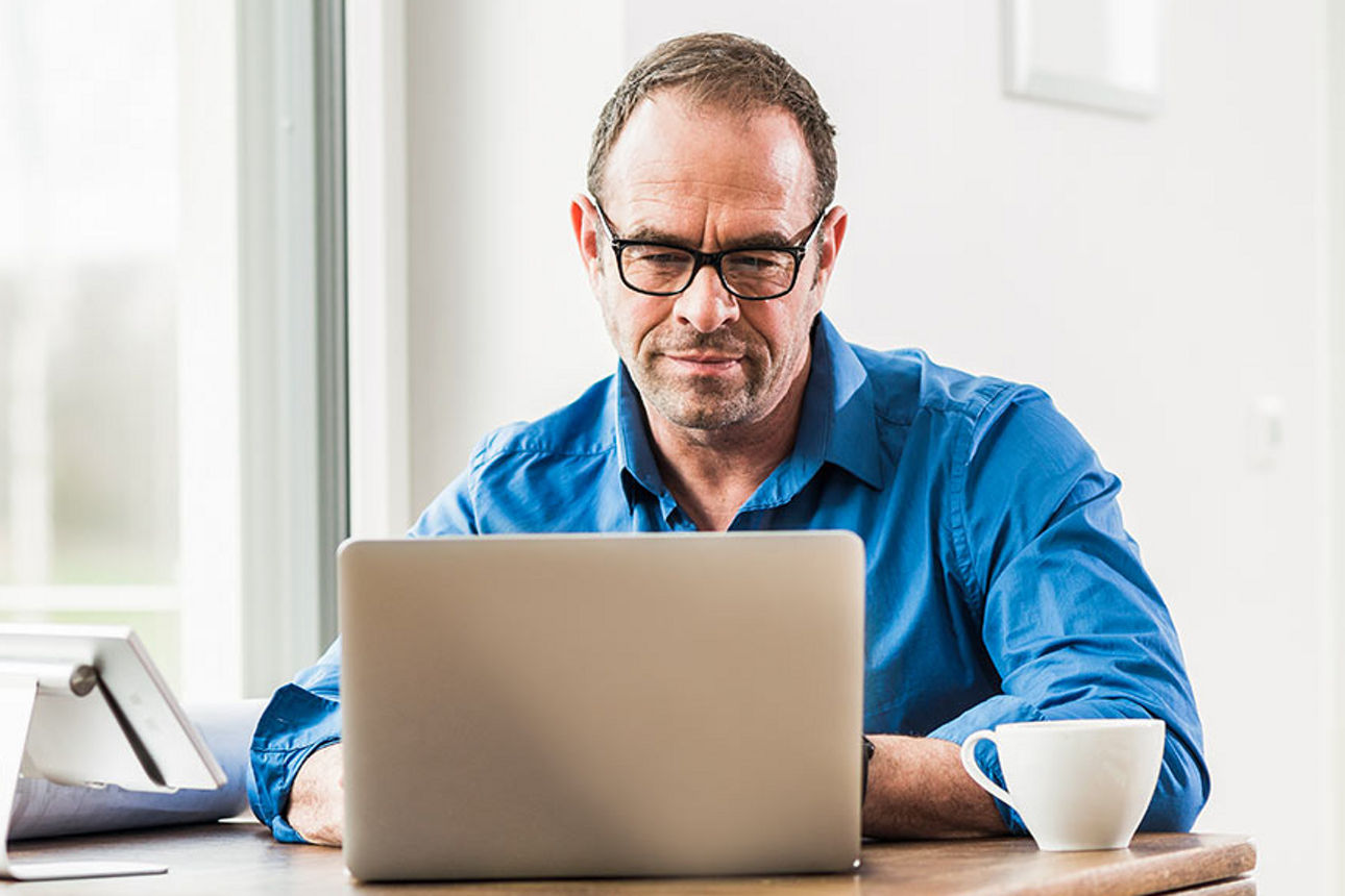 Mann sitzt am Tisch mit Laptop