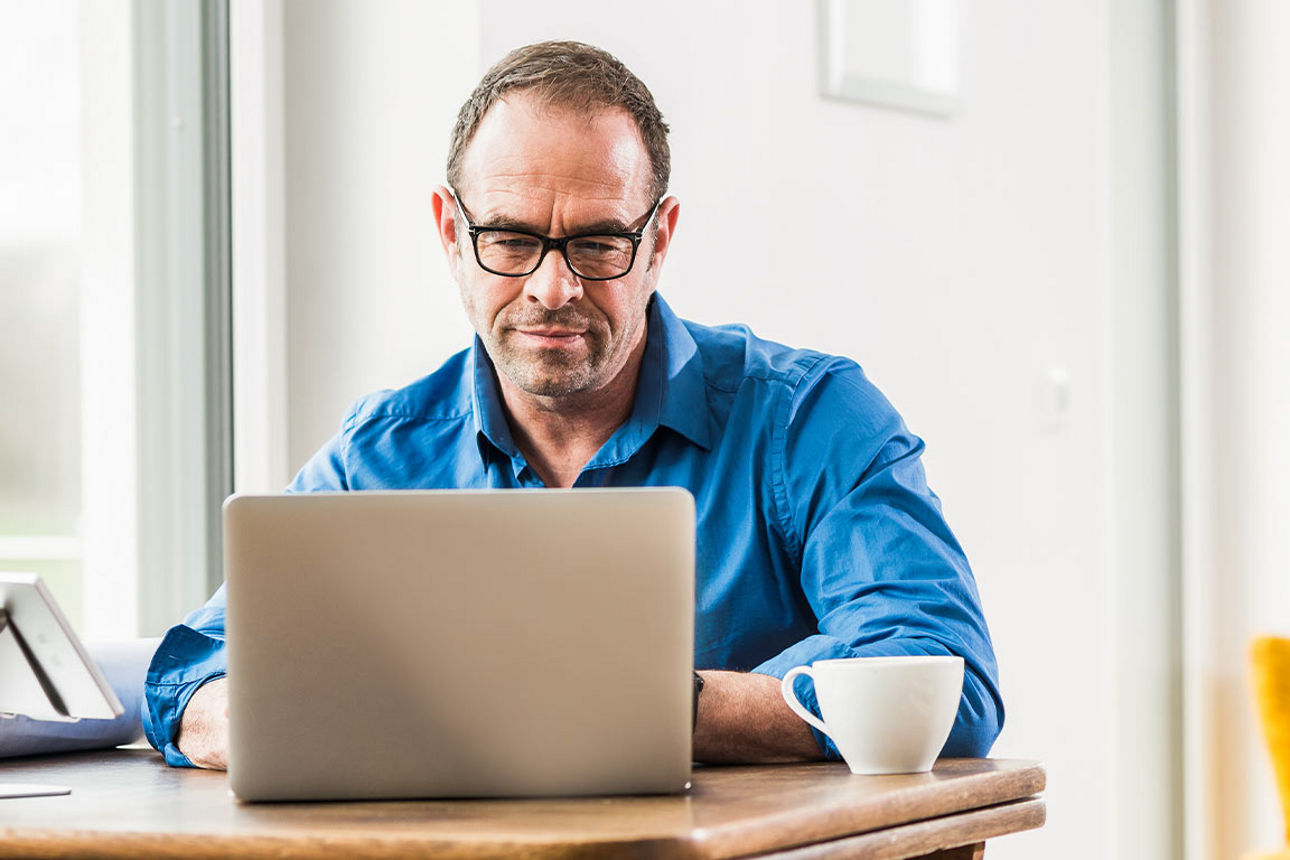 Mann mit blauem Hemd vor seinem Laptop sitzend.