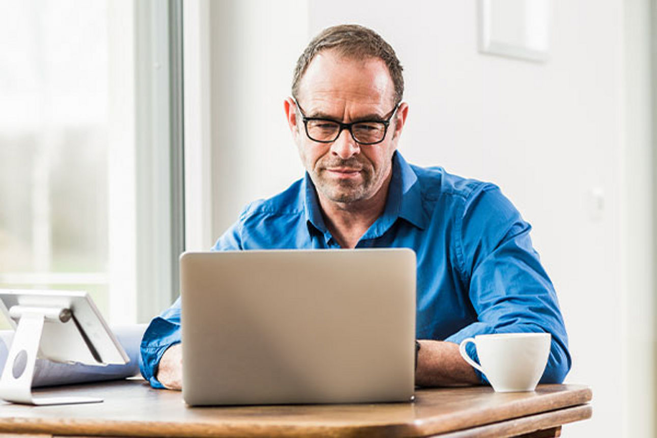 Mann sitzt vor einem Notebook am Schreibtisch.