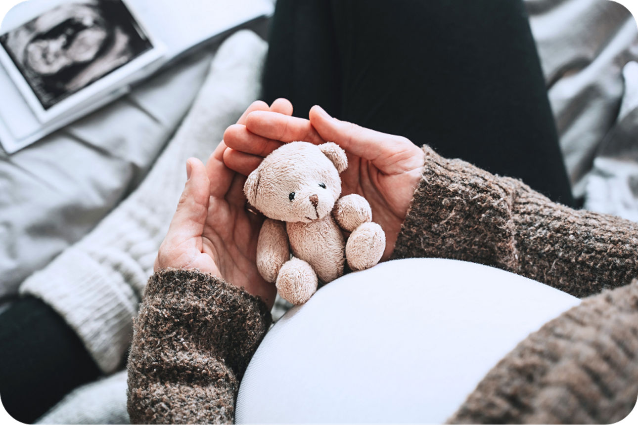 Schwangere Frau hält einen kleinen Teddybär