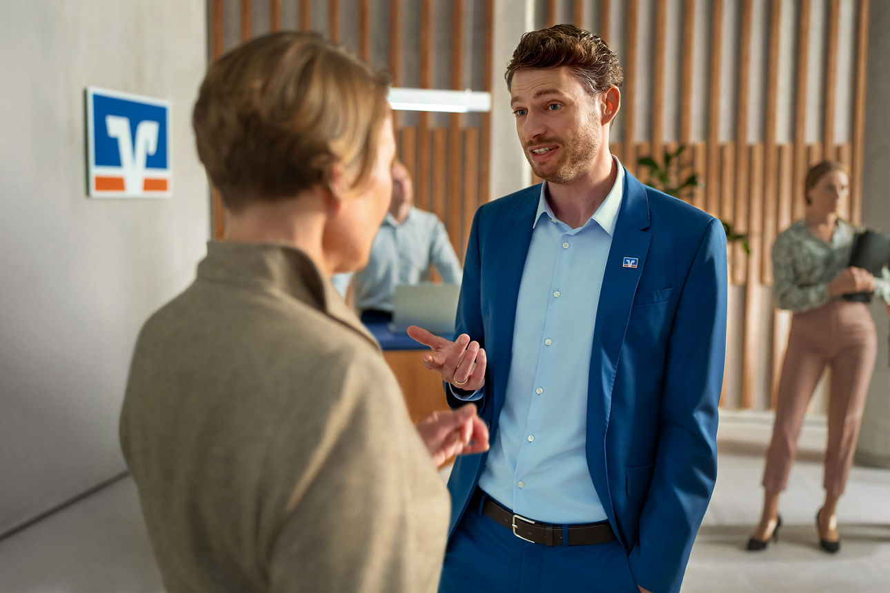 Zwei Personen stehen in einem modernen Bankfoyer und unterhalten sich.