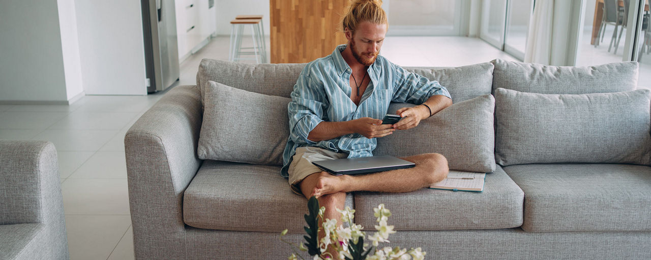 Mann sitzt mit einem Smartphone in der Hand auf seinem Sofa