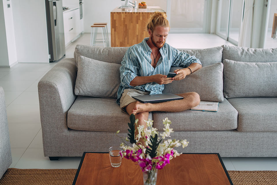 Mann sitzt mit einem Smartphone in der Hand auf seinem Sofa