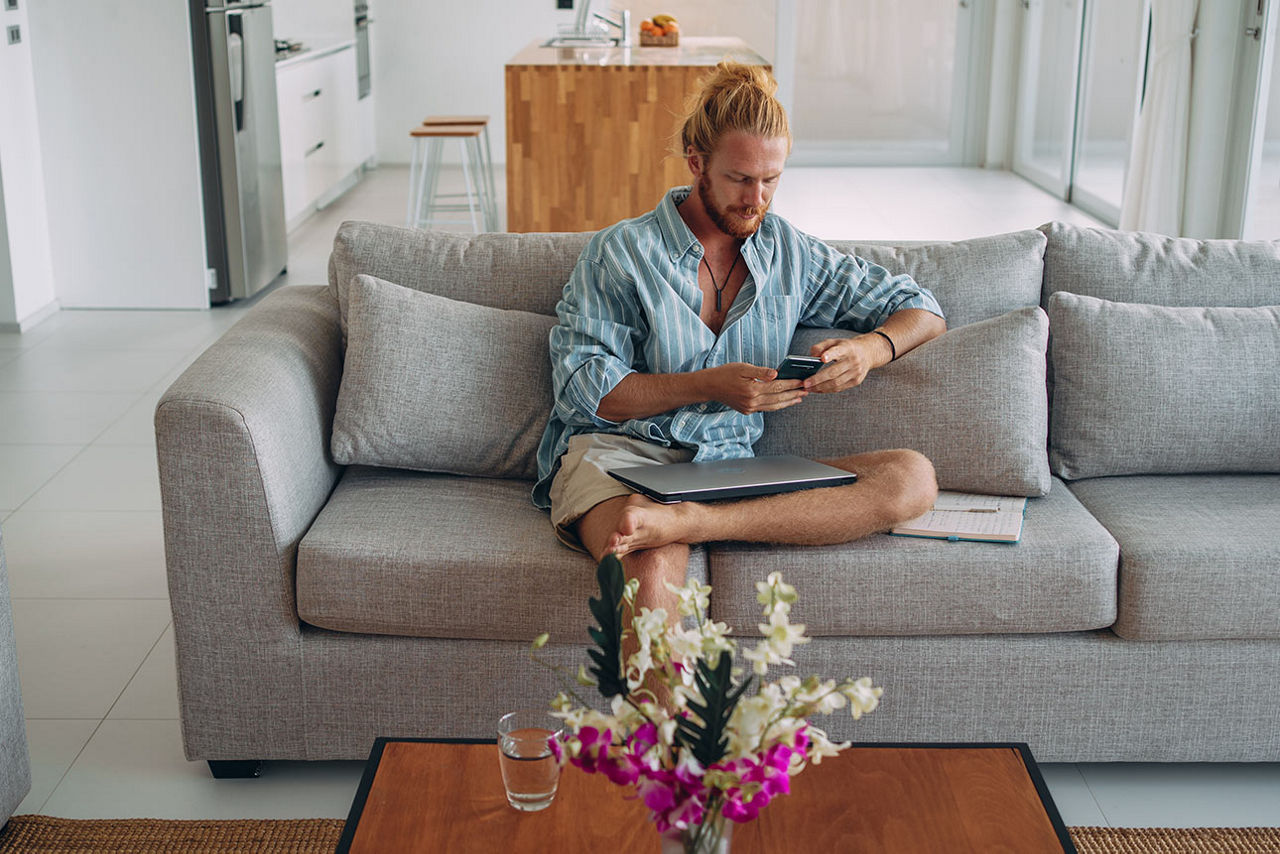 Mann sitzt mit einem Smartphone in der Hand auf seinem Sofa