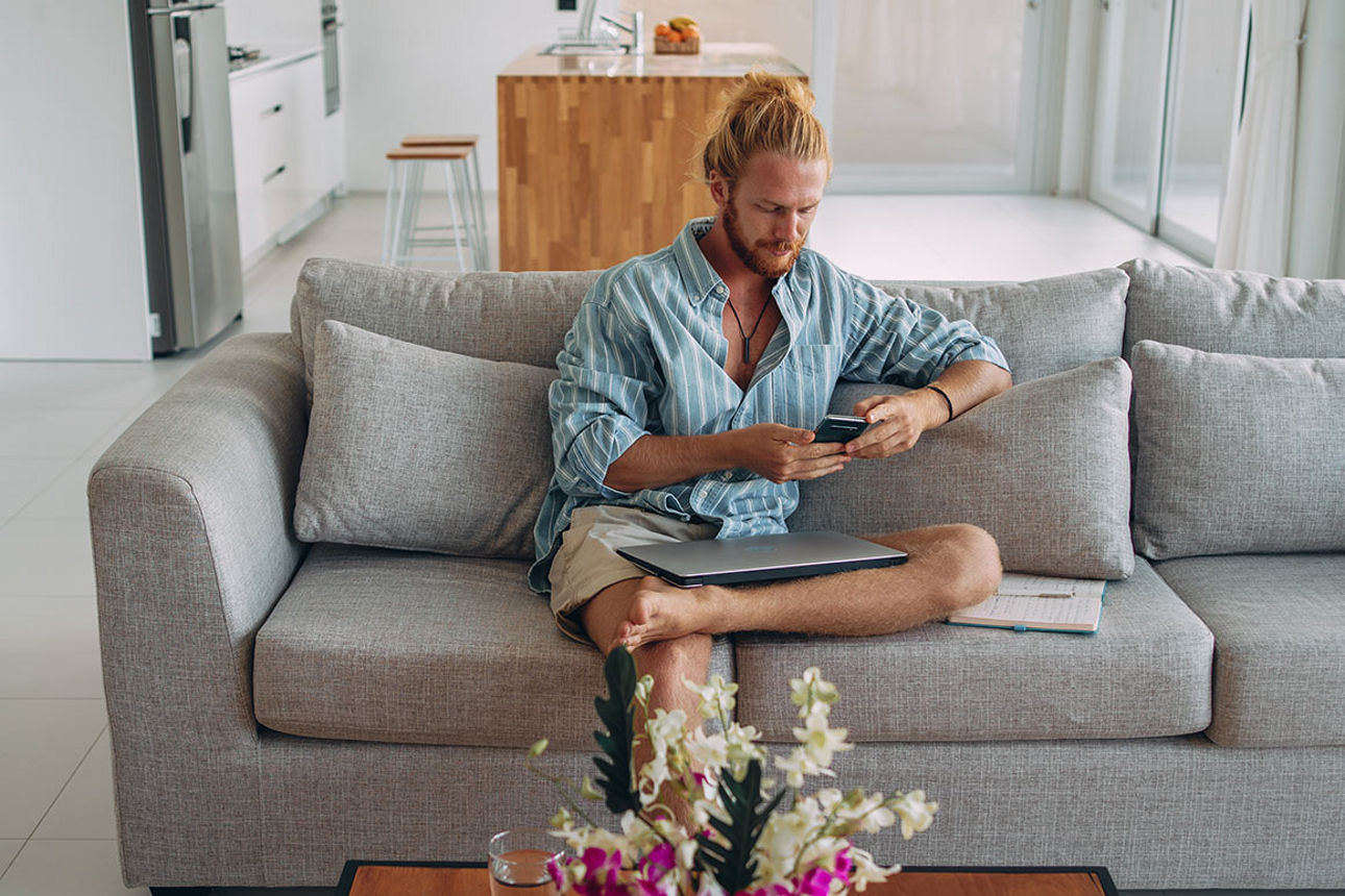 Mann sitzt mit einem Smartphone in der Hand auf seinem Sofa
