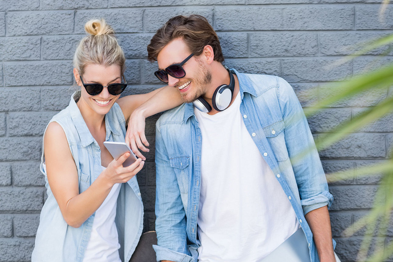 Paar mit Sonnenbrillen schaut gemeinsam auf ein Handy