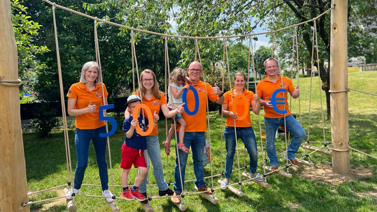 Fünf Mitarbeitende der Raiffeisenbank stehen auf einem Klettergerüst in einem Park und halten eine Summe von 5.000 € hoch