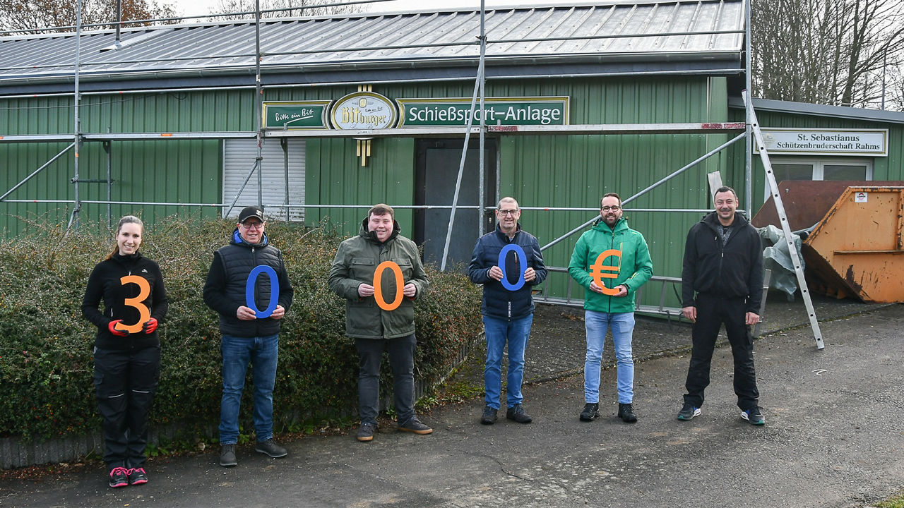 Mitglieder der Schützen Rahms und Mitarbeitende der Raiffeisenbank Neustadt eG stehen vor dem grünen Schützenhaus mit neuem Dach und Gerüst