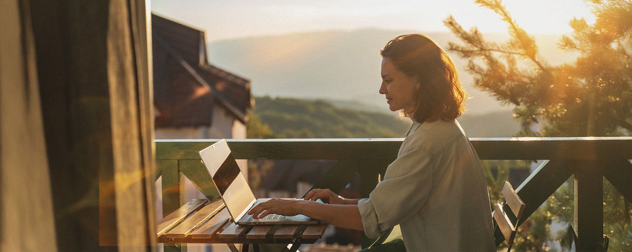 Junge Frau sitzt an ihrem Laptop auf dem Balkon