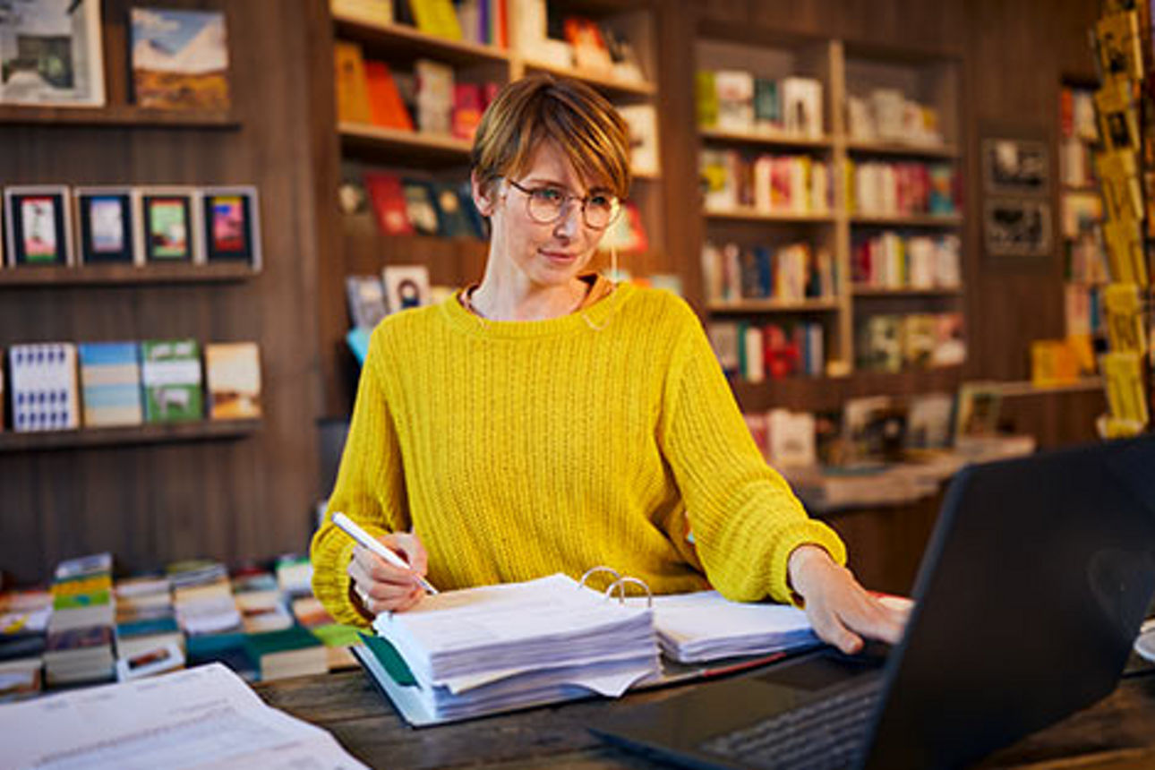 Frau mit Unterlagen und Laptop am Schreibtisch