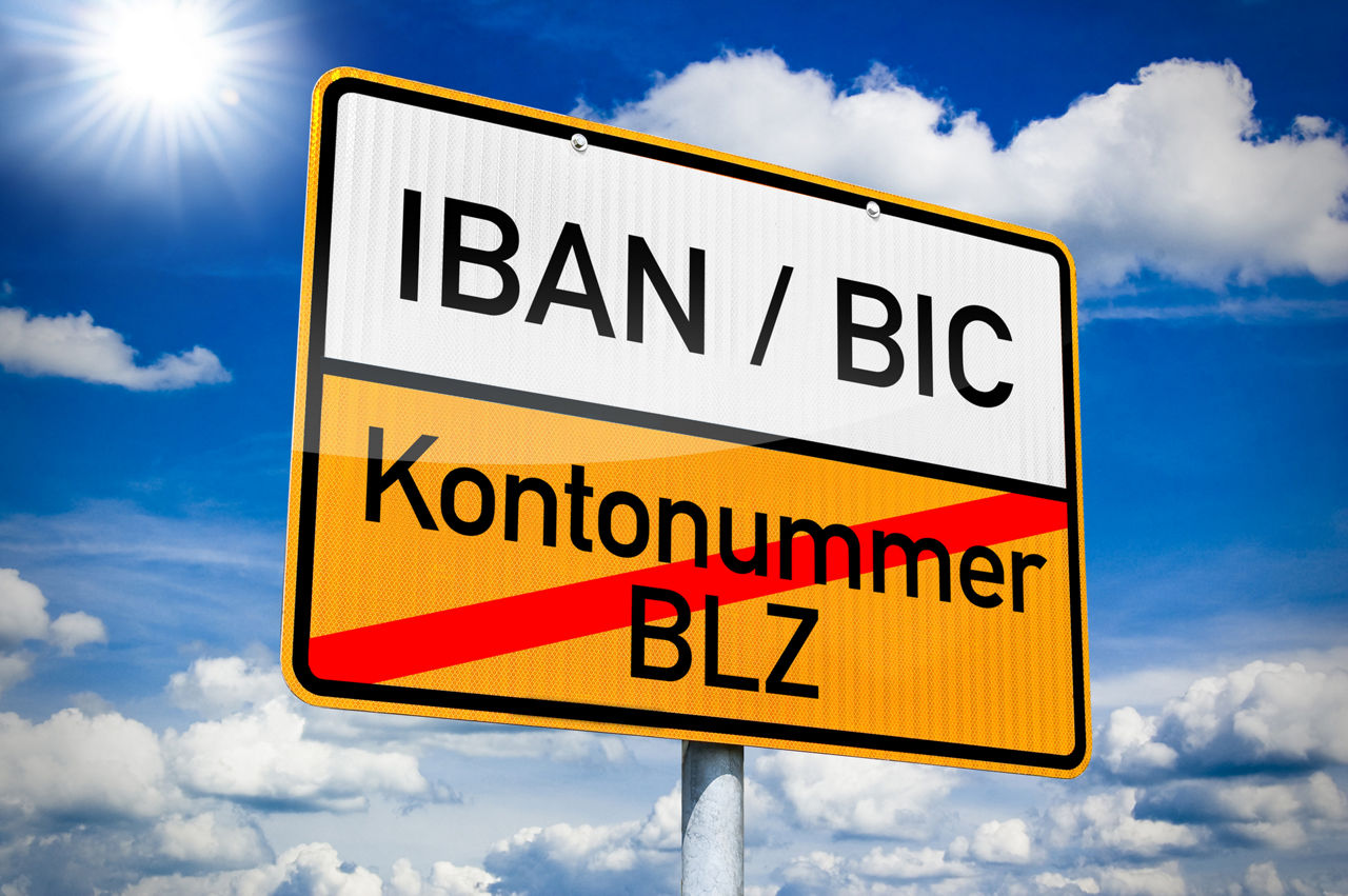 Ein Straßenschild auf dem IBAN / BIC geschrieben ist und Kontonummer / BLZ durchgestichen ist. 