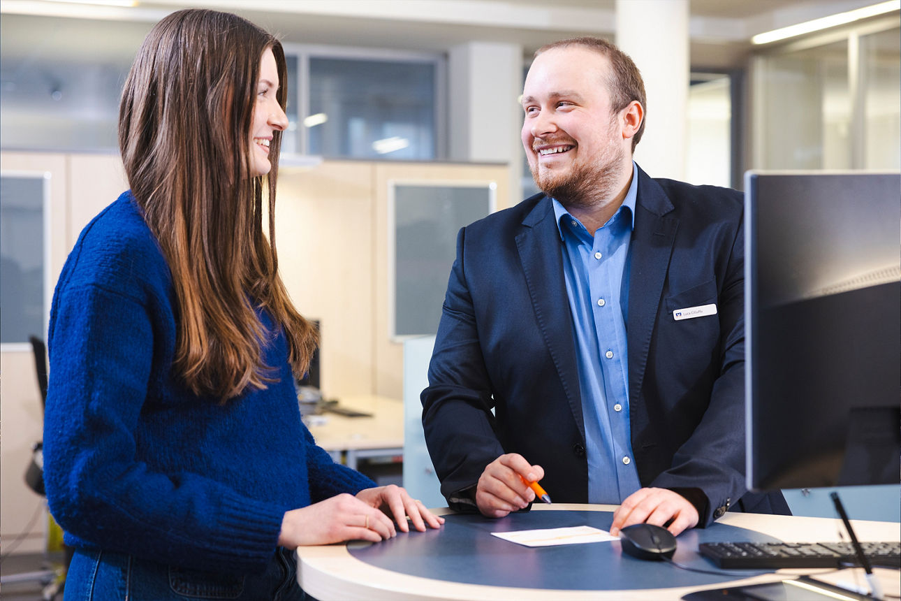 Bankberater und Kundin im Gespräch am Empfangstresen, freundliche Beratung im modernen Bankbüro.