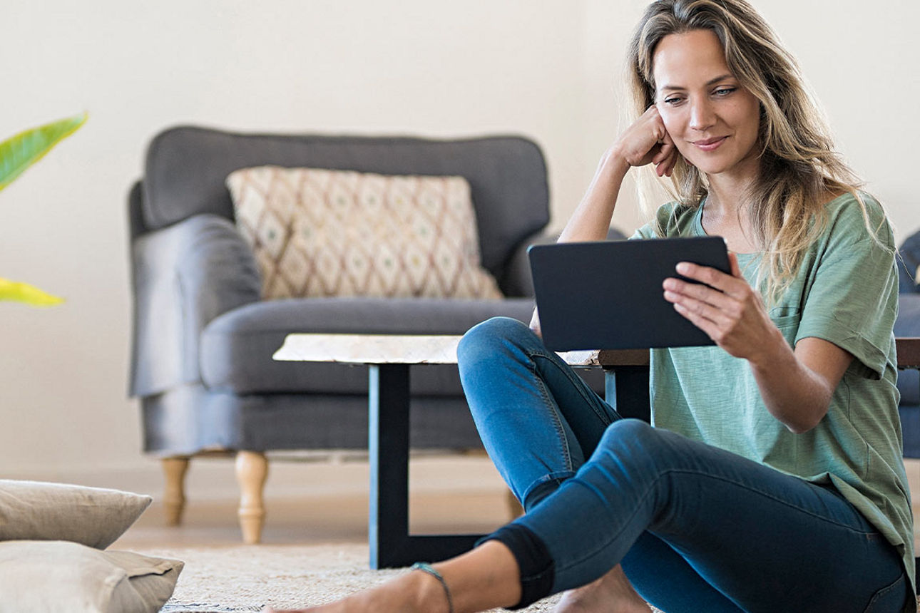 Junge Frau sitzt auf dem Boden des Wohnzimmers und schaut auf Ihr Tablet