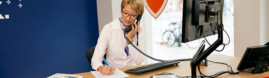 Bankmitarbeiterin telefoniert am Schreibtisch und macht sich Notizen