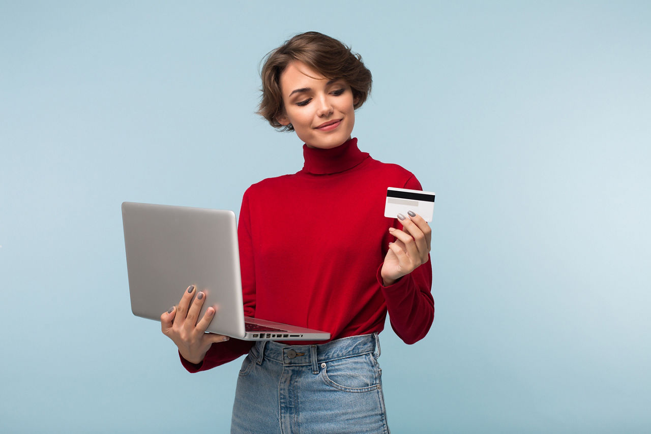 Ein junge Frau mit Laptop in einer Hand und einer Kreditkarte in der anderen Hand