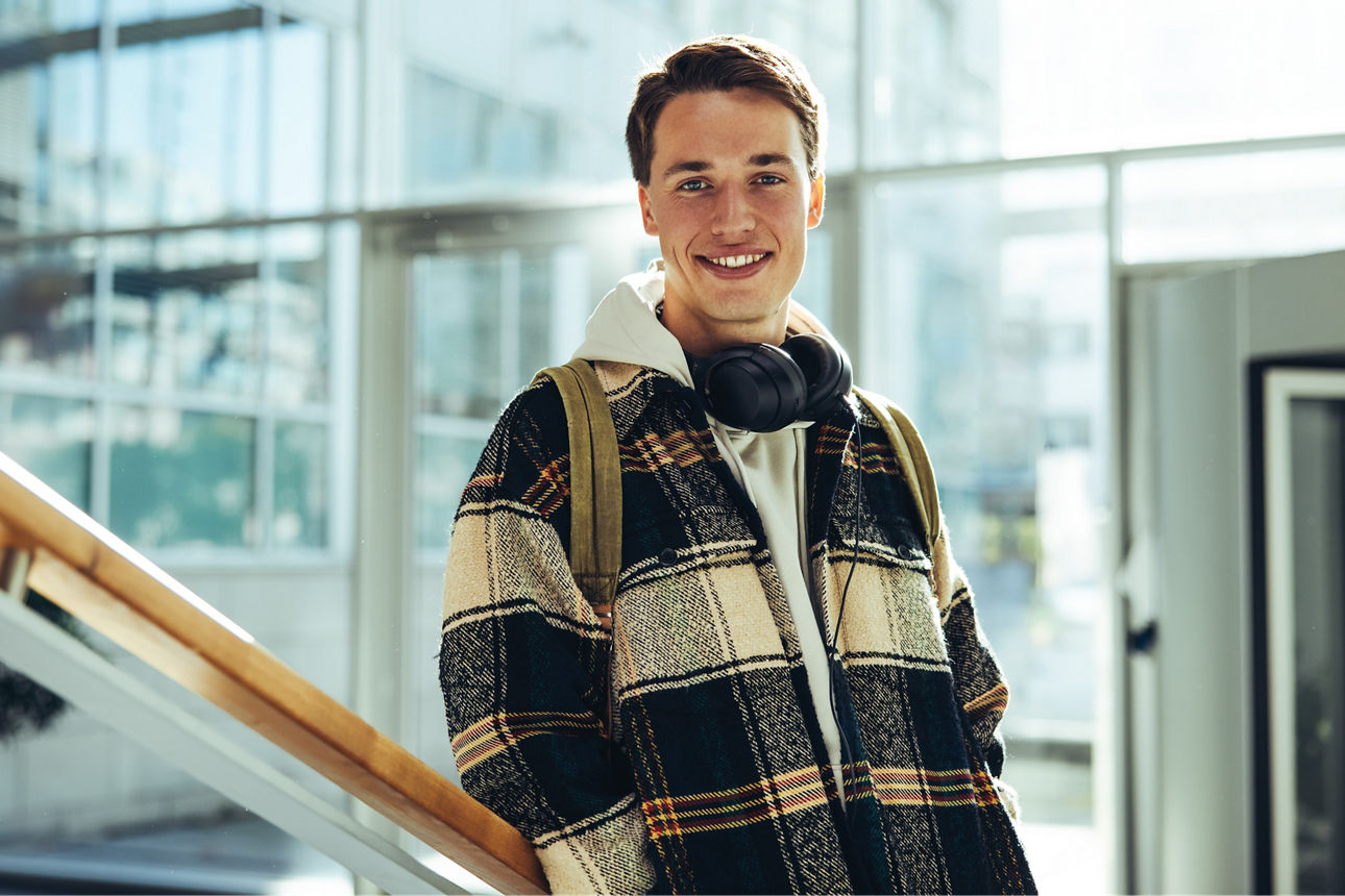 Ein junger mann mit Rucksack und Kopfhörern lächelt in die Kamera